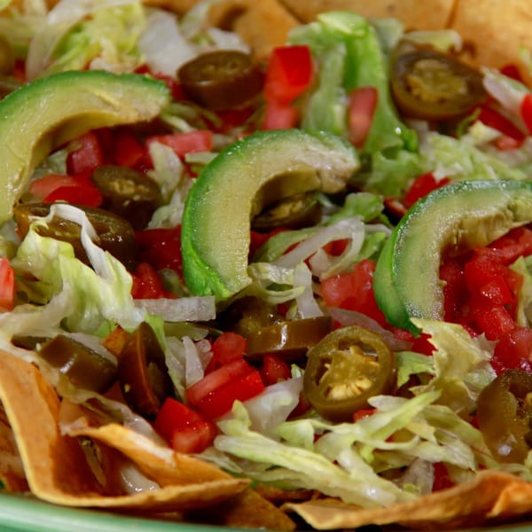 Close-up of crispy tortilla chips topped with lettuce, diced tomatoes, jalapeños, and avocado slices.
