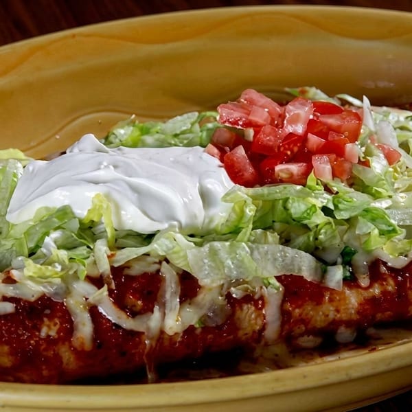 Two enchiladas covered in red sauce, melted cheese, shredded lettuce, diced tomatoes, and sour cream.