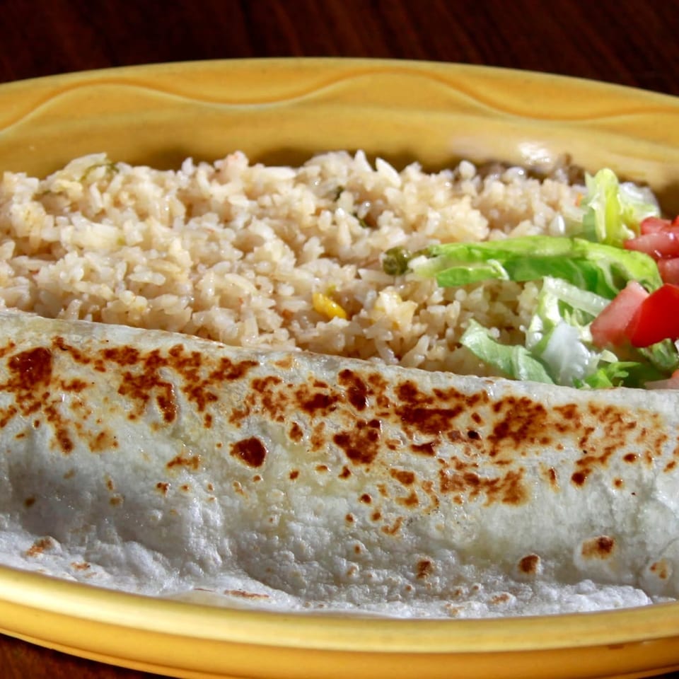 Grilled burrito served with seasoned rice, lettuce, diced tomatoes, onions, and sour cream on a decorative plate.