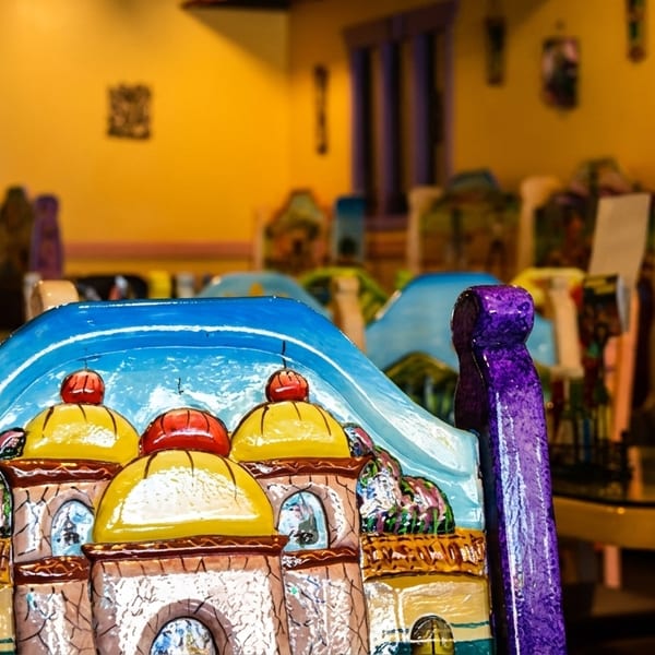 Colorful, hand-painted chairs with village scenes and sunflowers in a vibrant Mexican restaurant dining room.