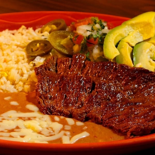 Carne asada with rice, refried beans, avocado, pico de gallo, and jalapeños on a red plate.