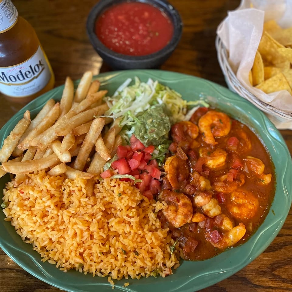 Mexican seafood platter with shrimp in red sauce, rice, fries, salad, guacamole, salsa, tortilla chips, and a Modelo beer.