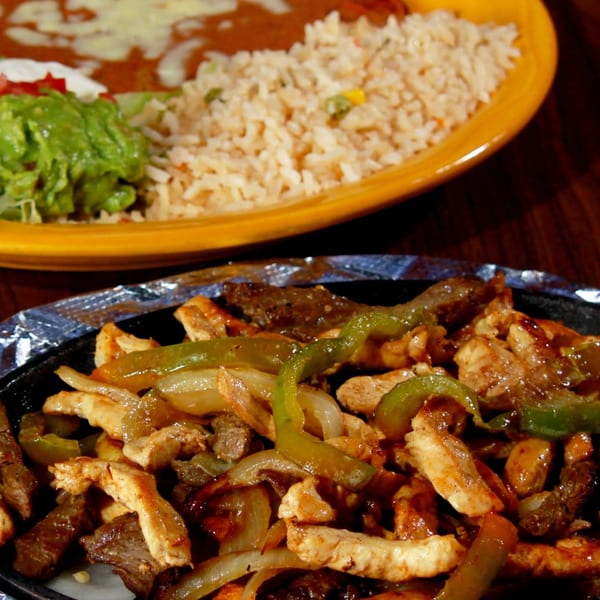 sizzling fajitas with grilled chicken, steak, peppers, and onions, served with rice, beans, guacamole, and salad