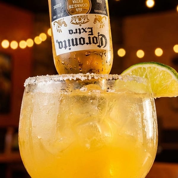 A Corona Extra bottle inverted into a salted margarita glass with a lime wedge, in a restaurant.